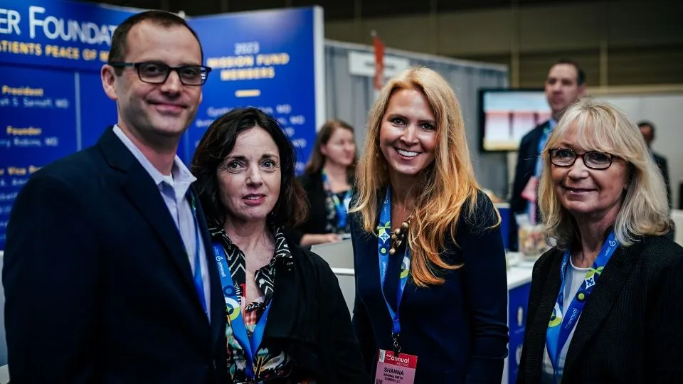 Three Symbio team members smiling together for a group photo at their exhibition booth during the AAD 2023 dermatology conference.